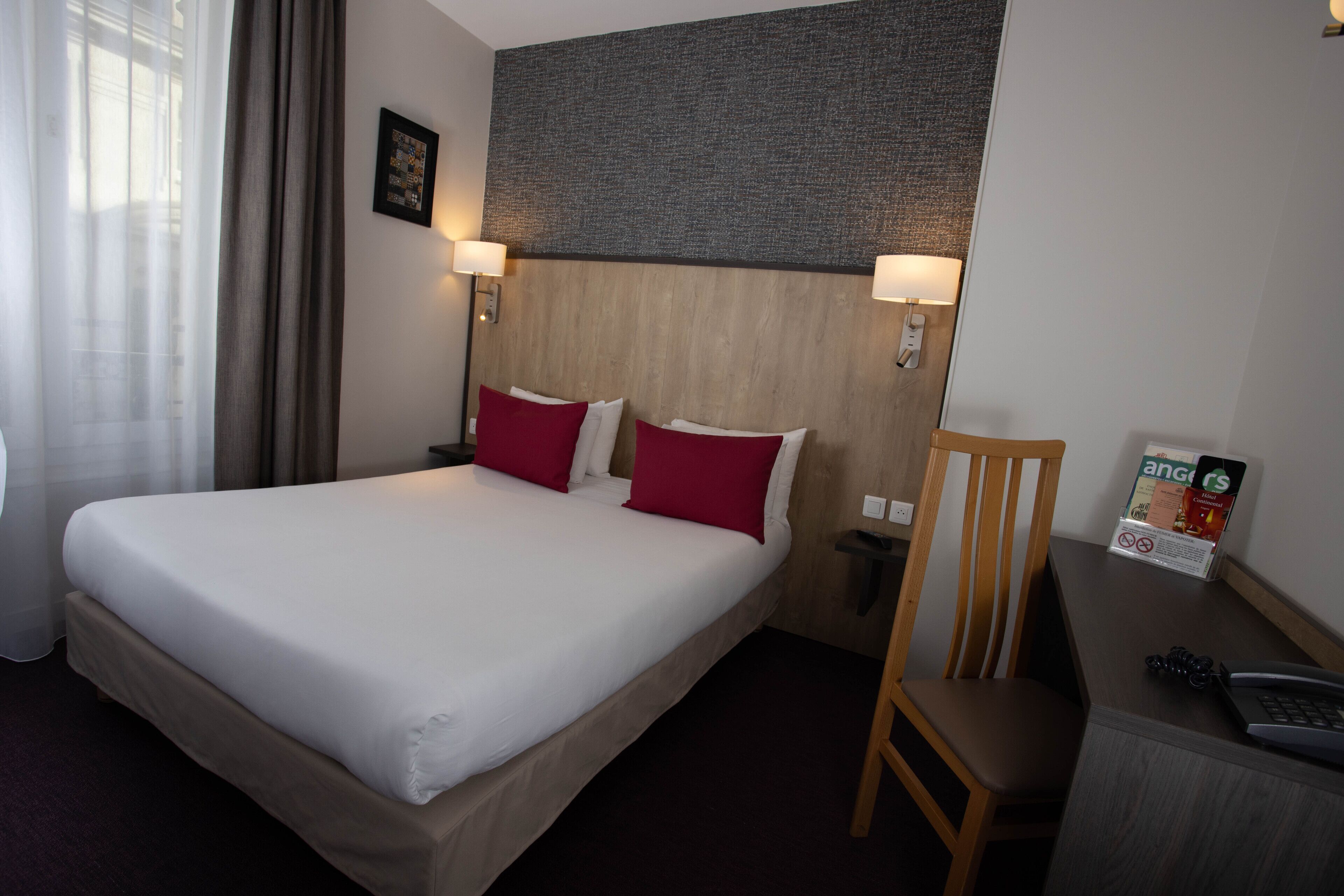 A hotel room with a large bed, two bedside lamps, a wooden headboard, a desk with a chair, and a framed picture on the wall.