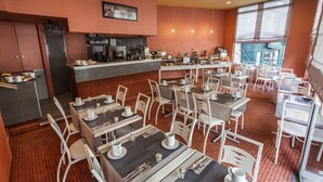 Un restaurante con varias mesas y sillas, una zona de cocina y ventanas amplias.