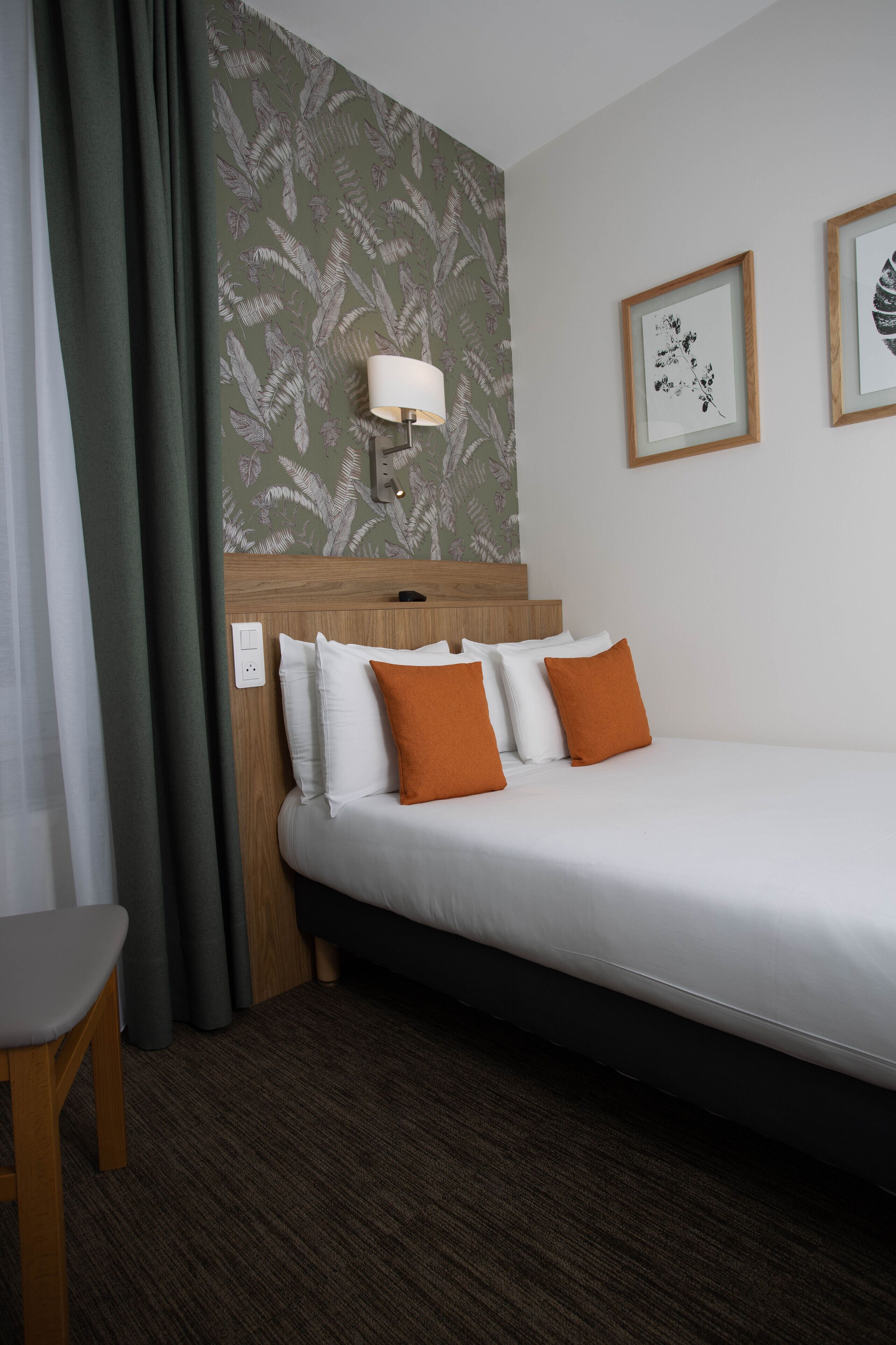 Ein Hotelzimmer mit einem Bett, einem Nachttisch, einer Lampe und einer Wand mit gerahmten Kunstwerken.