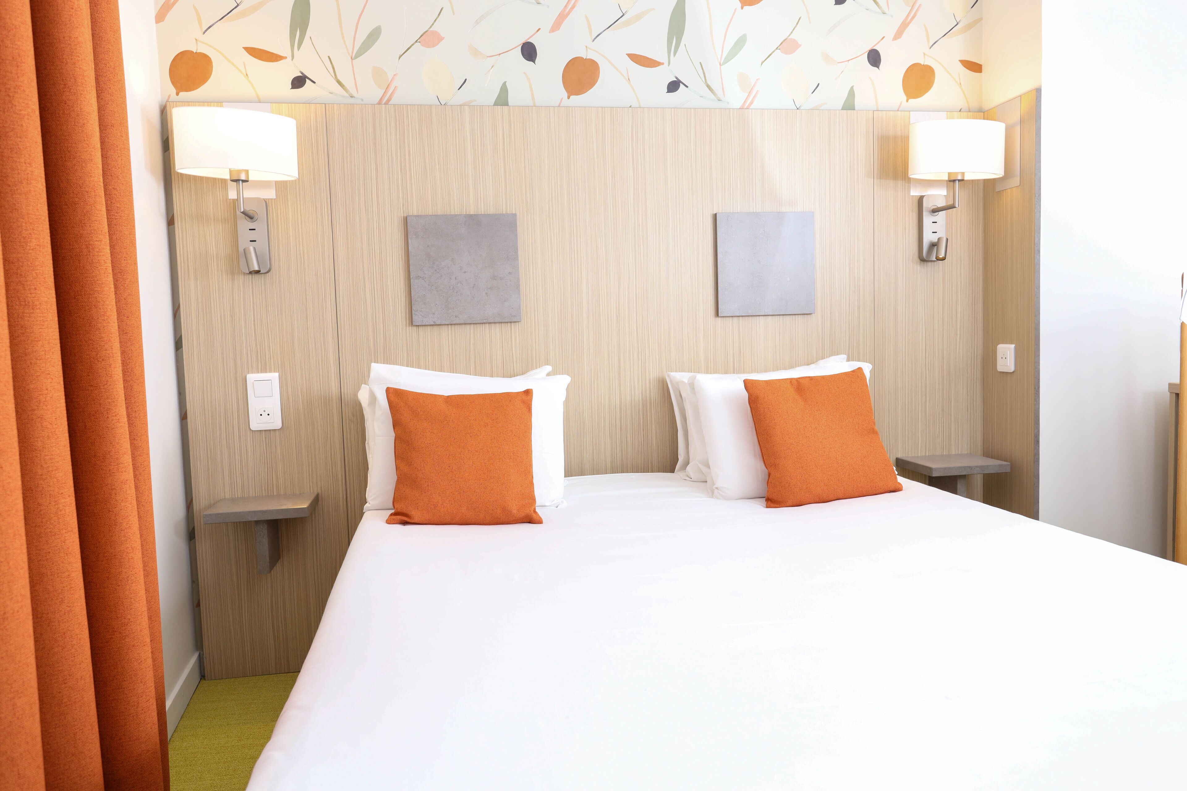 A hotel room with a large bed, two bedside tables, two lamps, and a wall with a leaf pattern.