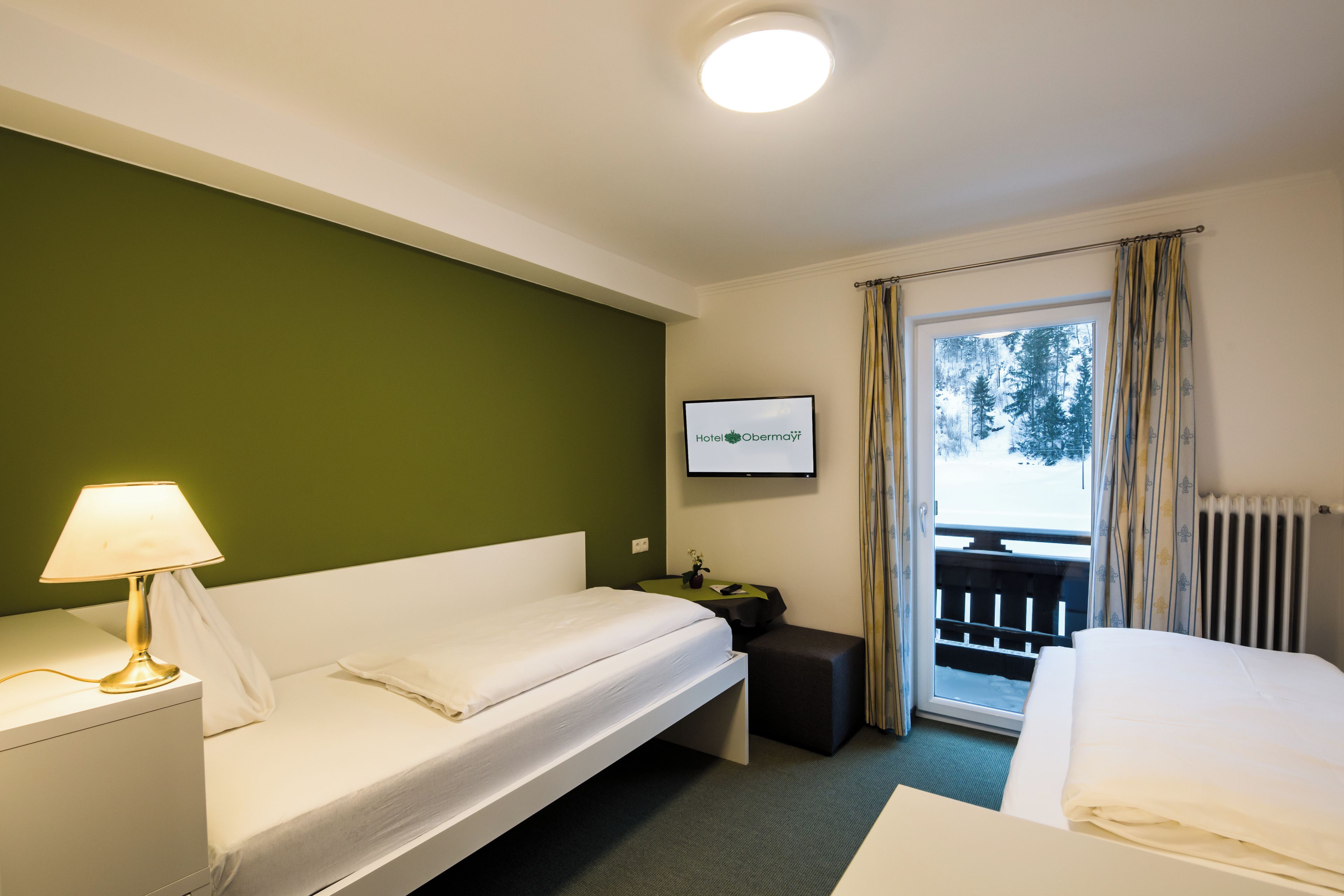 Una camera d'albergo con un letto, una scrivania, una sedia, una lampada, una televisione e una finestra con tende.