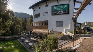 Un edificio con mesas al aire libre, un letrero que dice "Wirtshaus Zum Obermayer" y una montaña en el fondo.