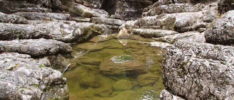 A natural rocky landscape with a clear water pool surrounded by large boulders.