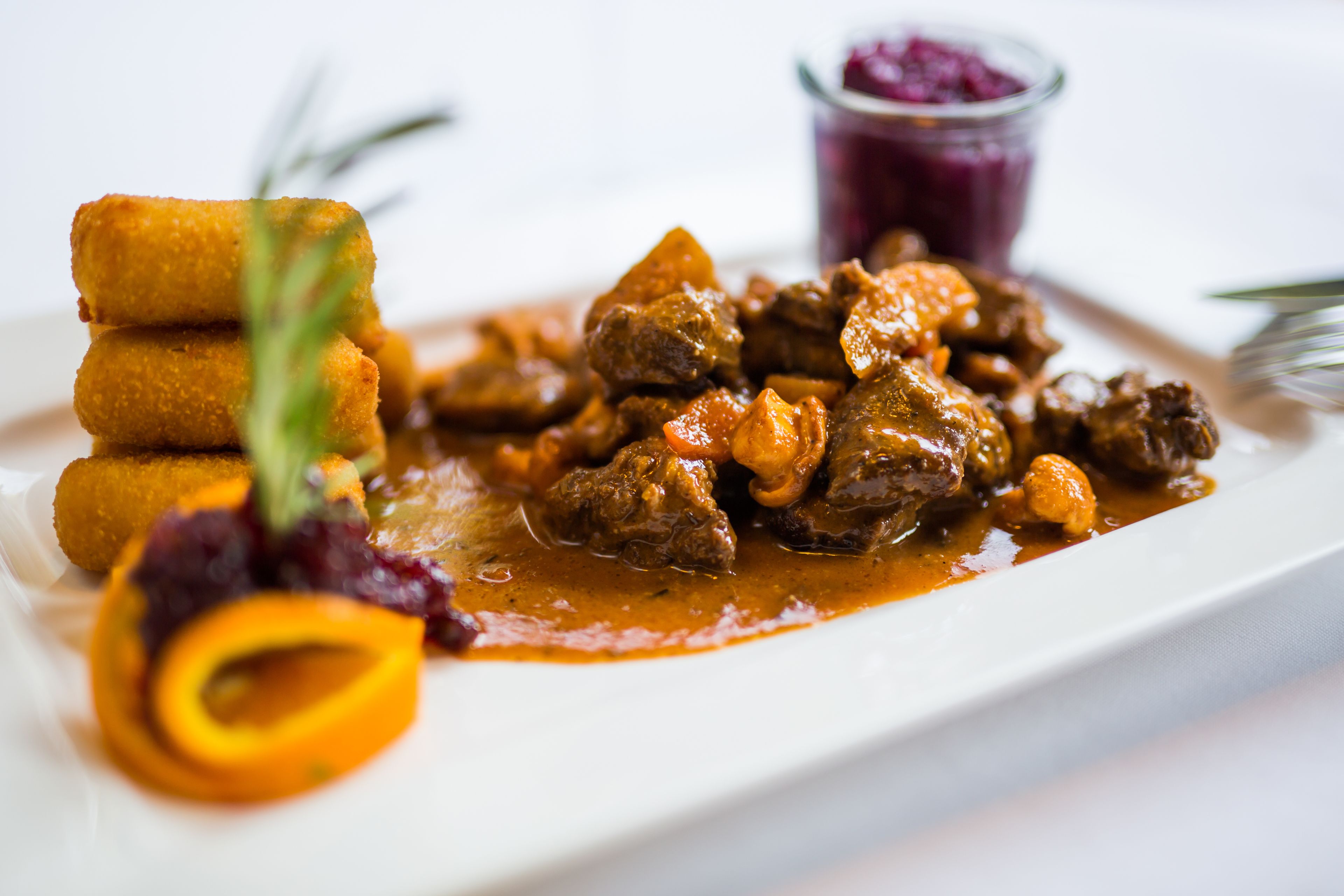 Un plato de comida con carne y verduras, acompañado de un recipiente pequeño de salsa y una rodaja de naranja decorativa.