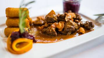 Un plato de comida con carne y verduras, acompañado de un recipiente pequeño de salsa y una rodaja de naranja decorativa.