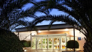 A building with a glass entrance, surrounded by palm trees and a well-lit lawn. - Parador de Ayamonte (Ayamonte)