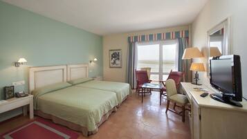 Una habitación de hotel con cama, escritorio con televisor, silla y ventana con cortinas.