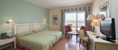 A hotel room with a bed, a desk with a TV, a chair, and a window with curtains.
