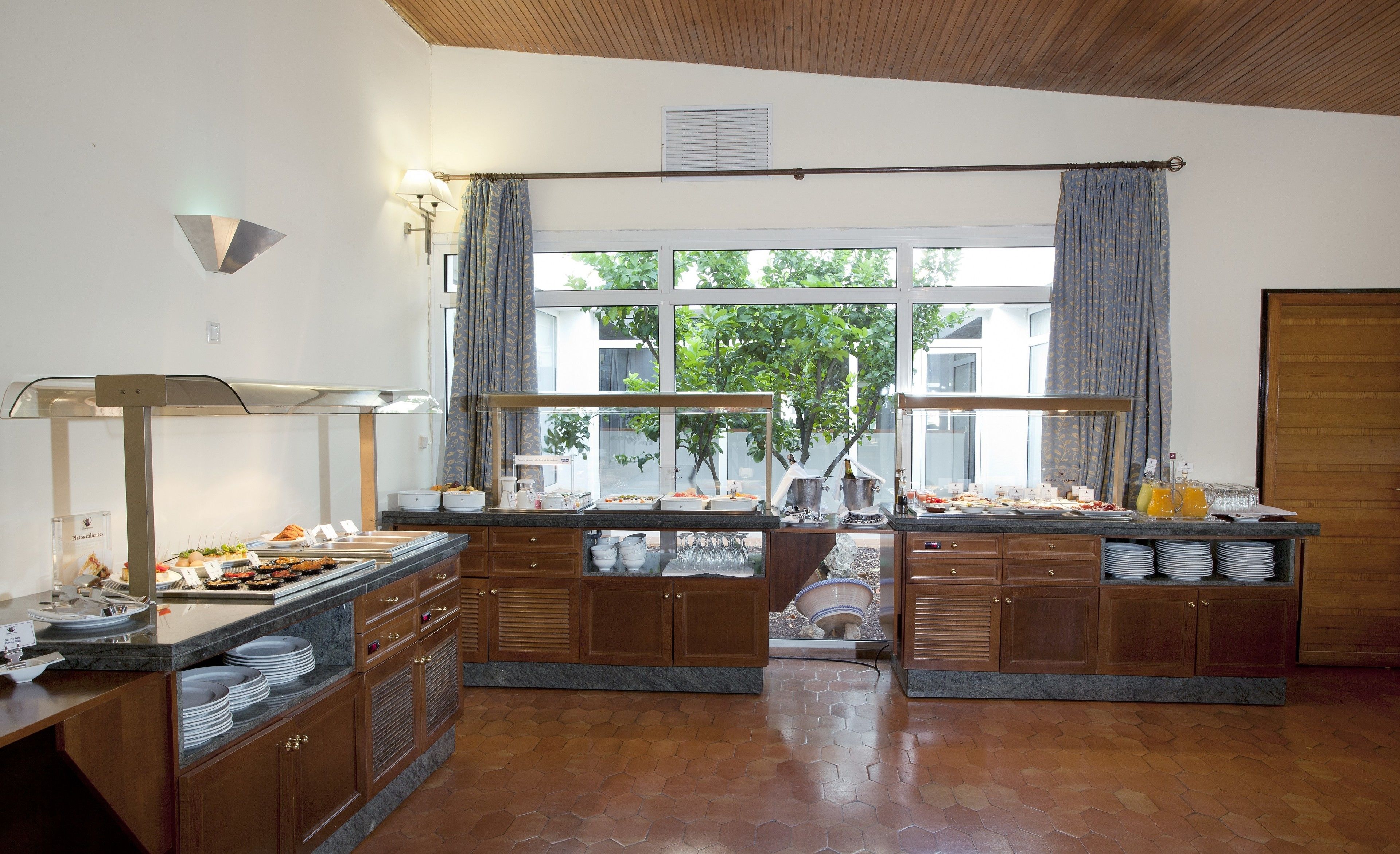 Una cocina con una disposición tipo bufé, armarios de madera y un amplio ventanal con cortinas.