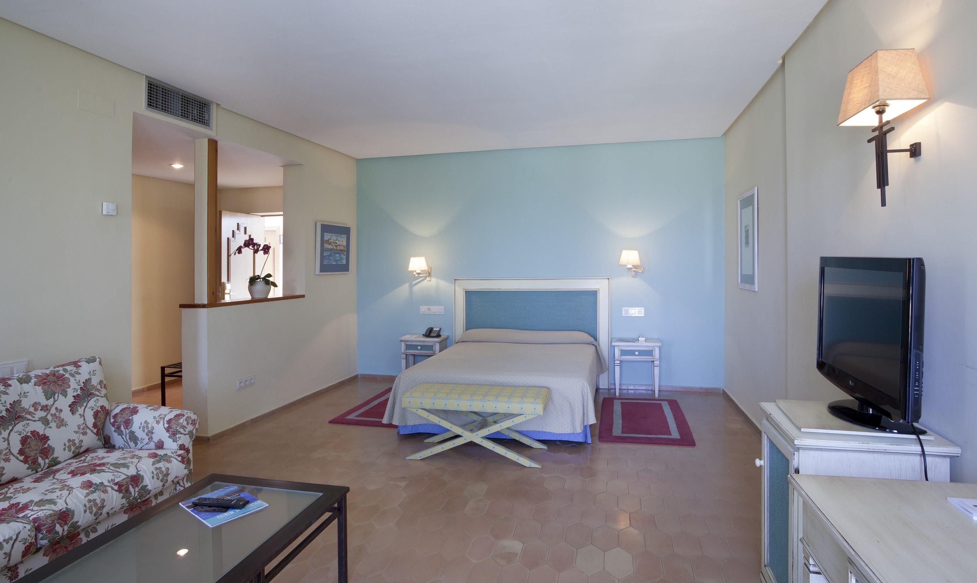 Una habitación de hotel con cama, televisión, sofá y una mesita.