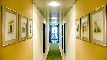 A hallway with framed artwork on the walls, a green carpet, and a ceiling light.