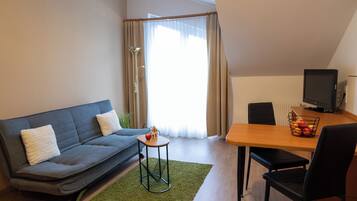 Una sala moderna con un sofá gris, una mesita redonda con un modelo de casa, una mesa de comedor con sillas y una televisión.