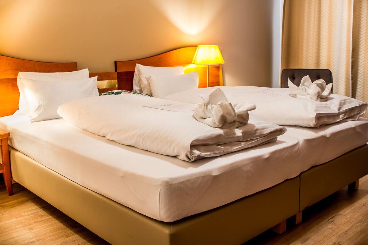 A neatly made bed with white linens and decorative pillows, a bedside lamp, and a wooden nightstand.