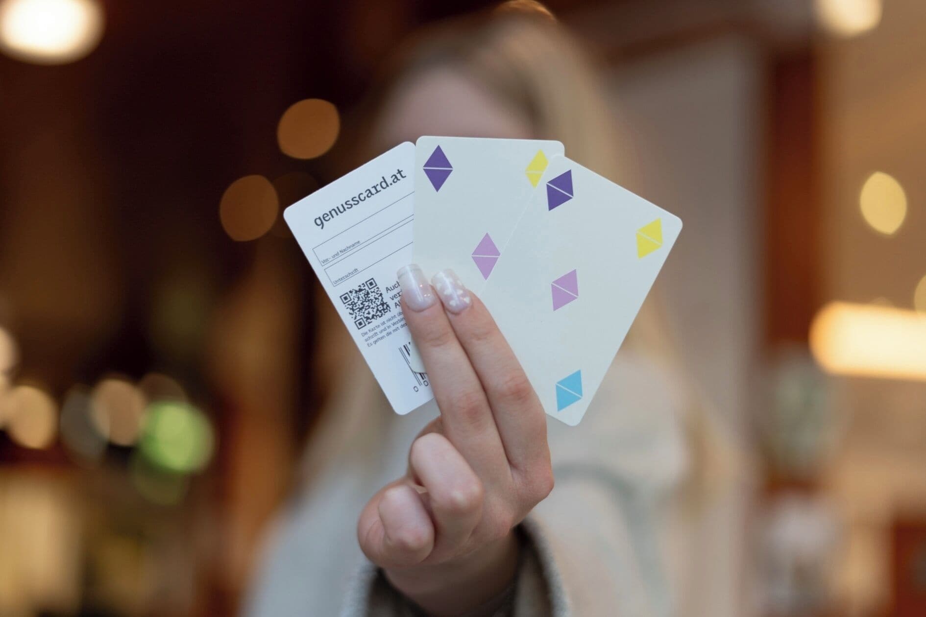 Eine Person hält eine Karte mit einem QR-Code und Text, im Hintergrund verschwommene Lichter in einem Raum.