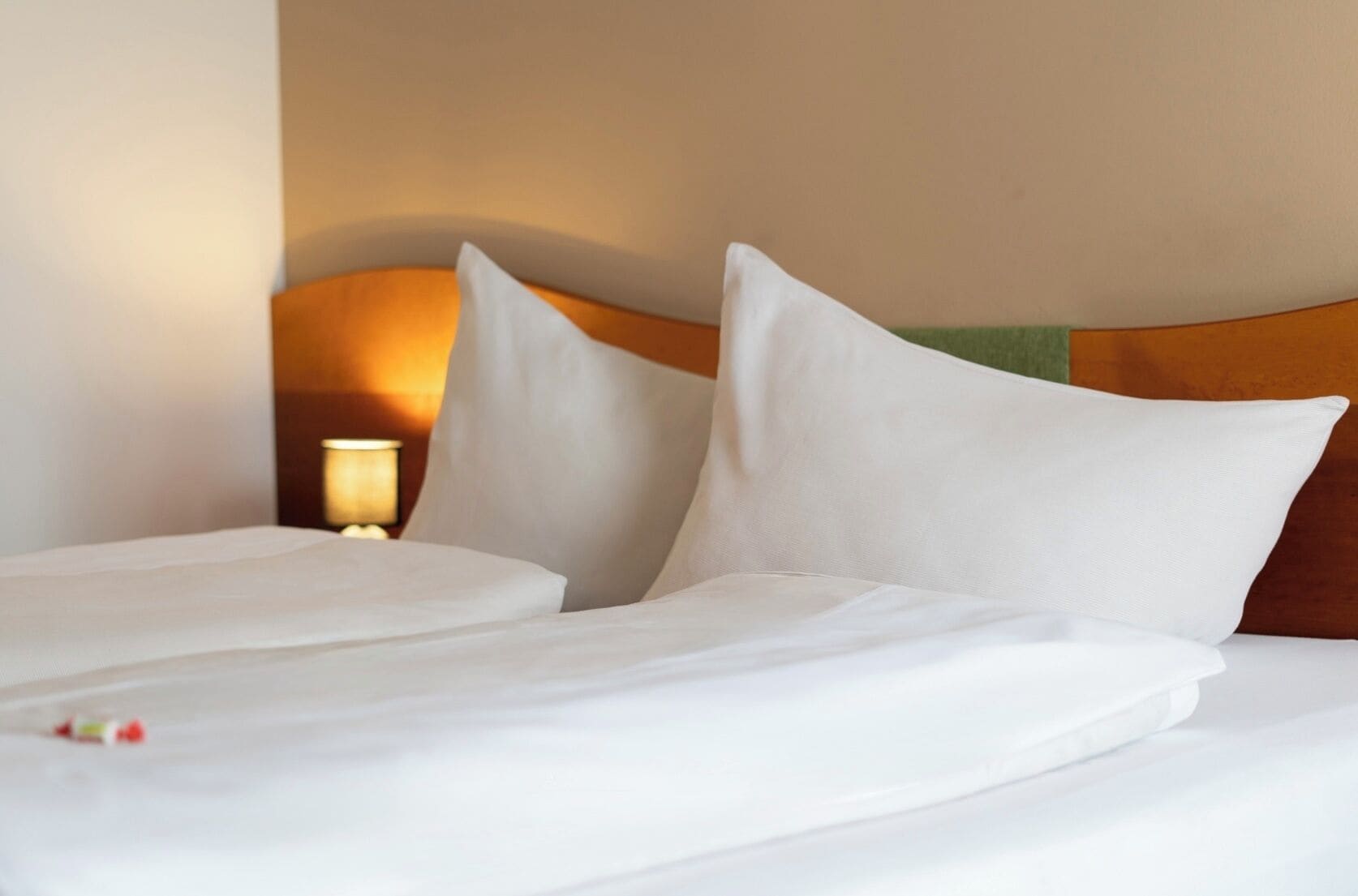 A neatly made bed with white linens and pillows, a wooden headboard, and a bedside lamp.