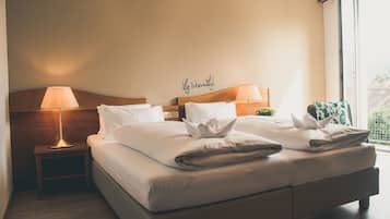 Un letto matrimoniale rifatto con lenzuola bianche, due lampade ai comodini e un cartello appeso al muro con la scritta "life is beautiful".