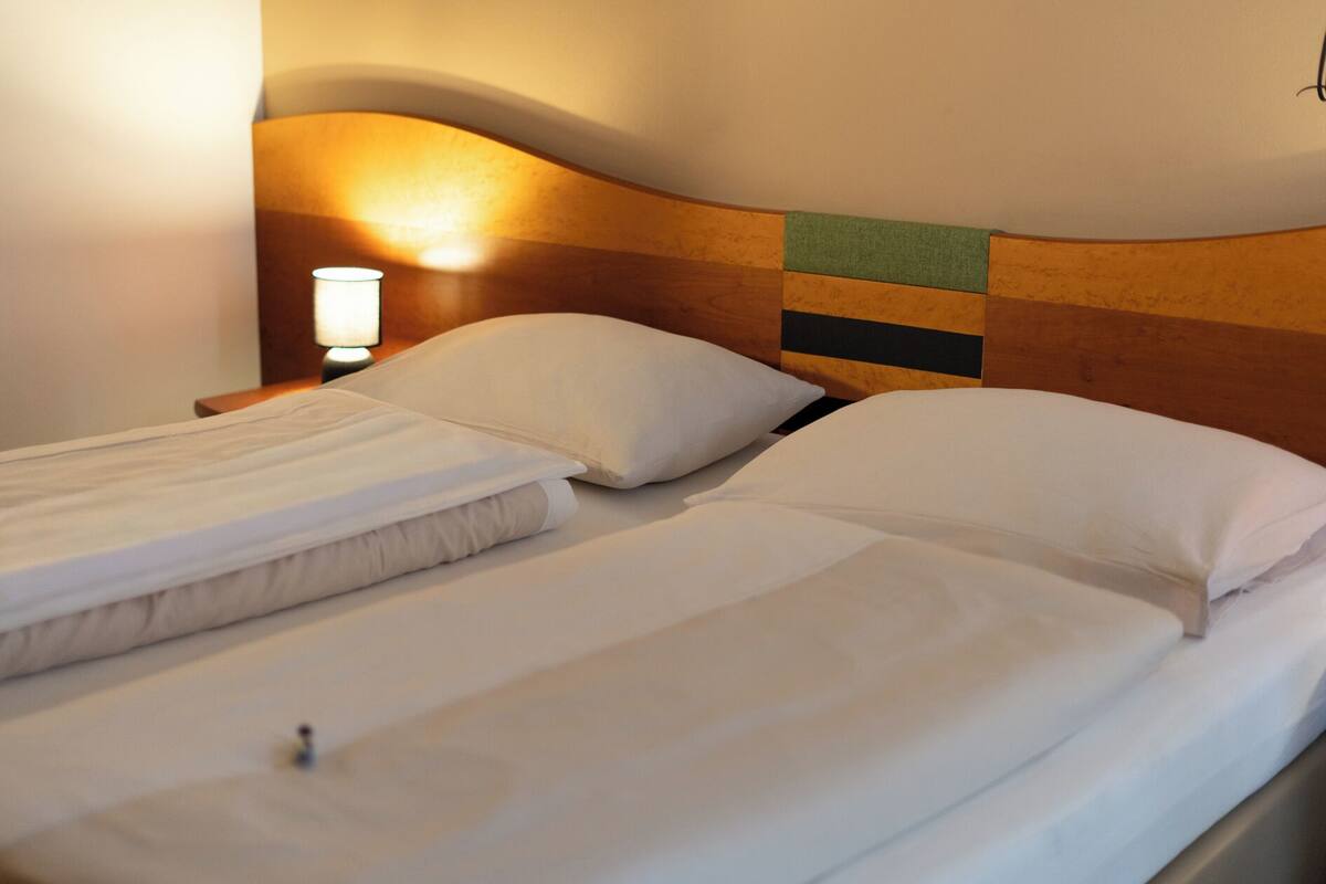 A double bed with white linens, a wooden headboard with a striped design, and a bedside lamp.