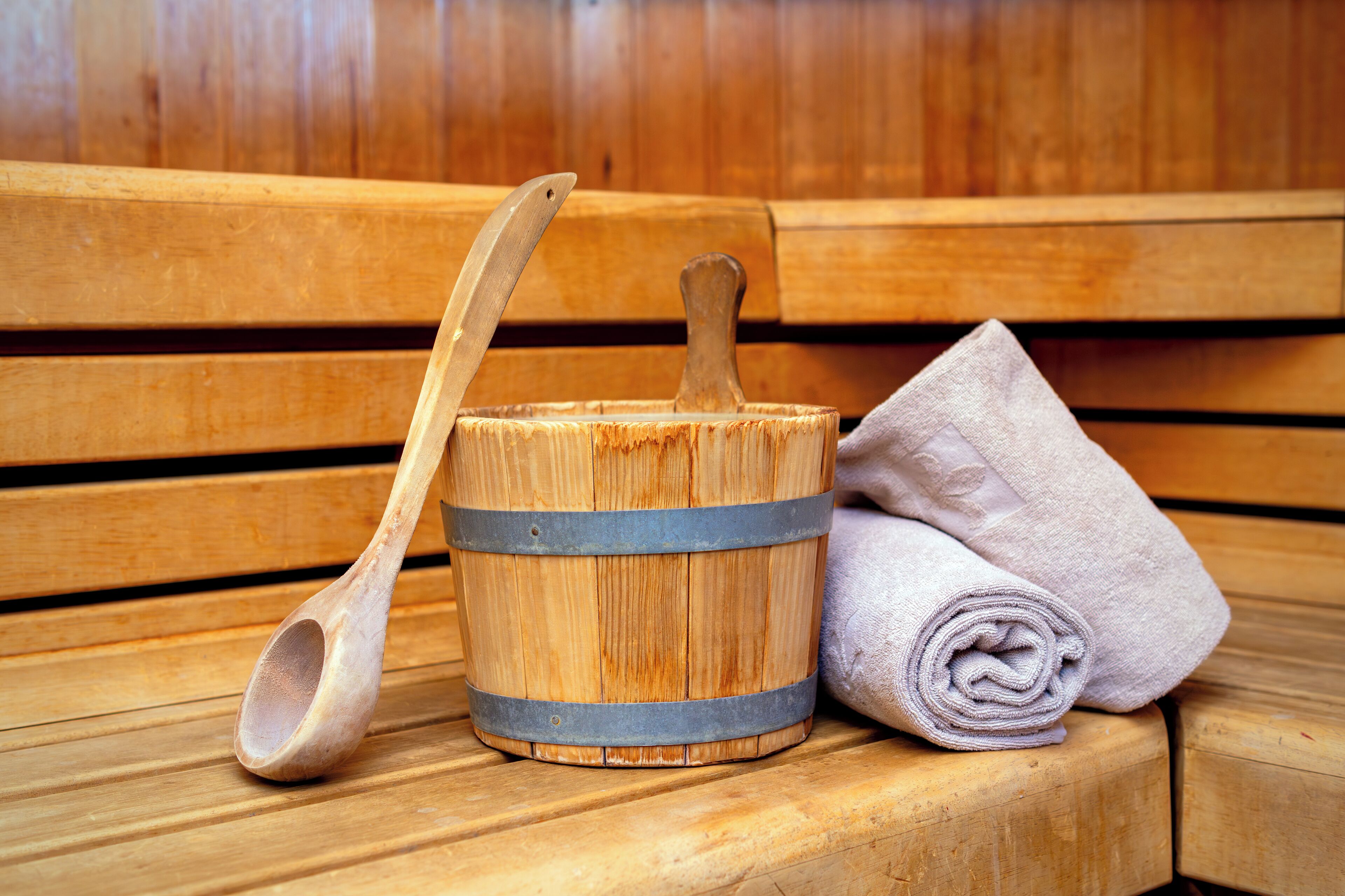 A wooden bench with a wooden bucket and a rolled towel on it.