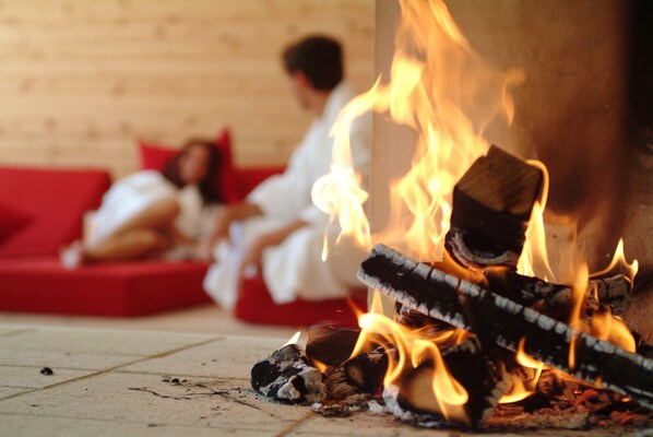 A room with a fire, a red couch, and a person in white clothing.