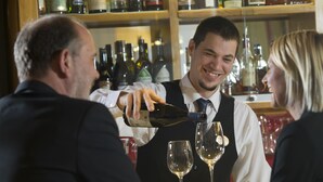 A bartender pouring a drink into a wine glass at a bar.
