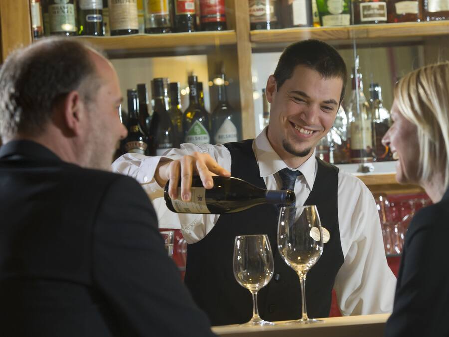 Un cantinero sirviendo una bebida en una copa de vino en un bar.