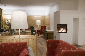 A modern living room with wooden panel walls, a fireplace, and red patterned furniture. - SPA Hotel Erzherzog Johann (Bad Aussee)