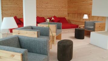 Un interior moderno con paneles de madera, sofás tapizados en gris, cojines rojos y un otomán pequeño y redondo.