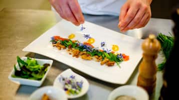 A chef plating a dish with various garnishes and a small bowl of greens.