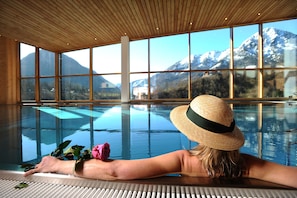 Une personne se détend au bord d’une piscine, avec une vue sur les montagnes à travers de grandes fenêtres.