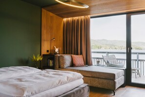 A modern bedroom with a large bed, a sofa, and a balcony with a view of the hills.