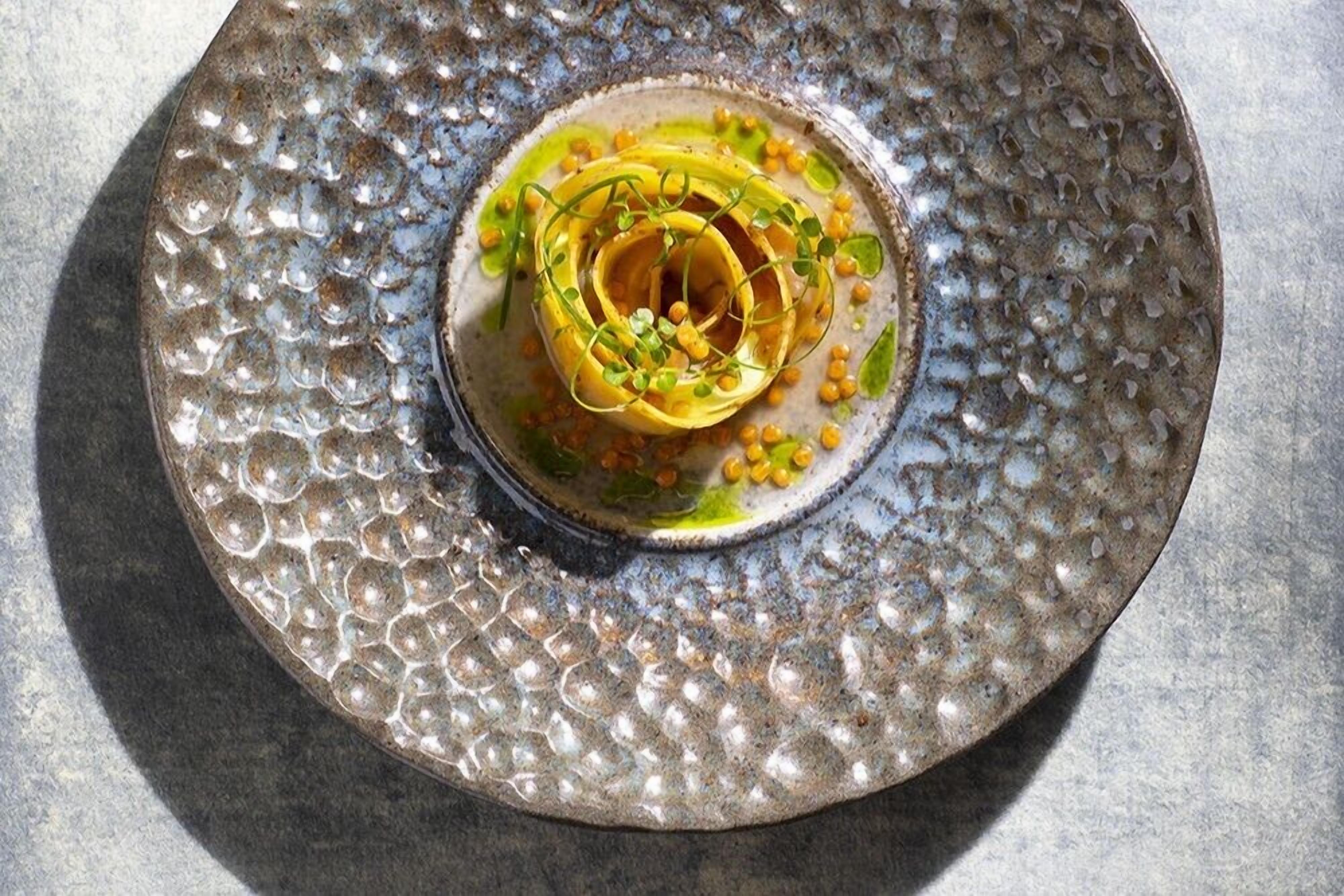 A textured, round ceramic plate with a central spiral design and green garnish.