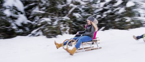A person in a winter setting, wearing a hat and jacket, seated on a sled-like device.