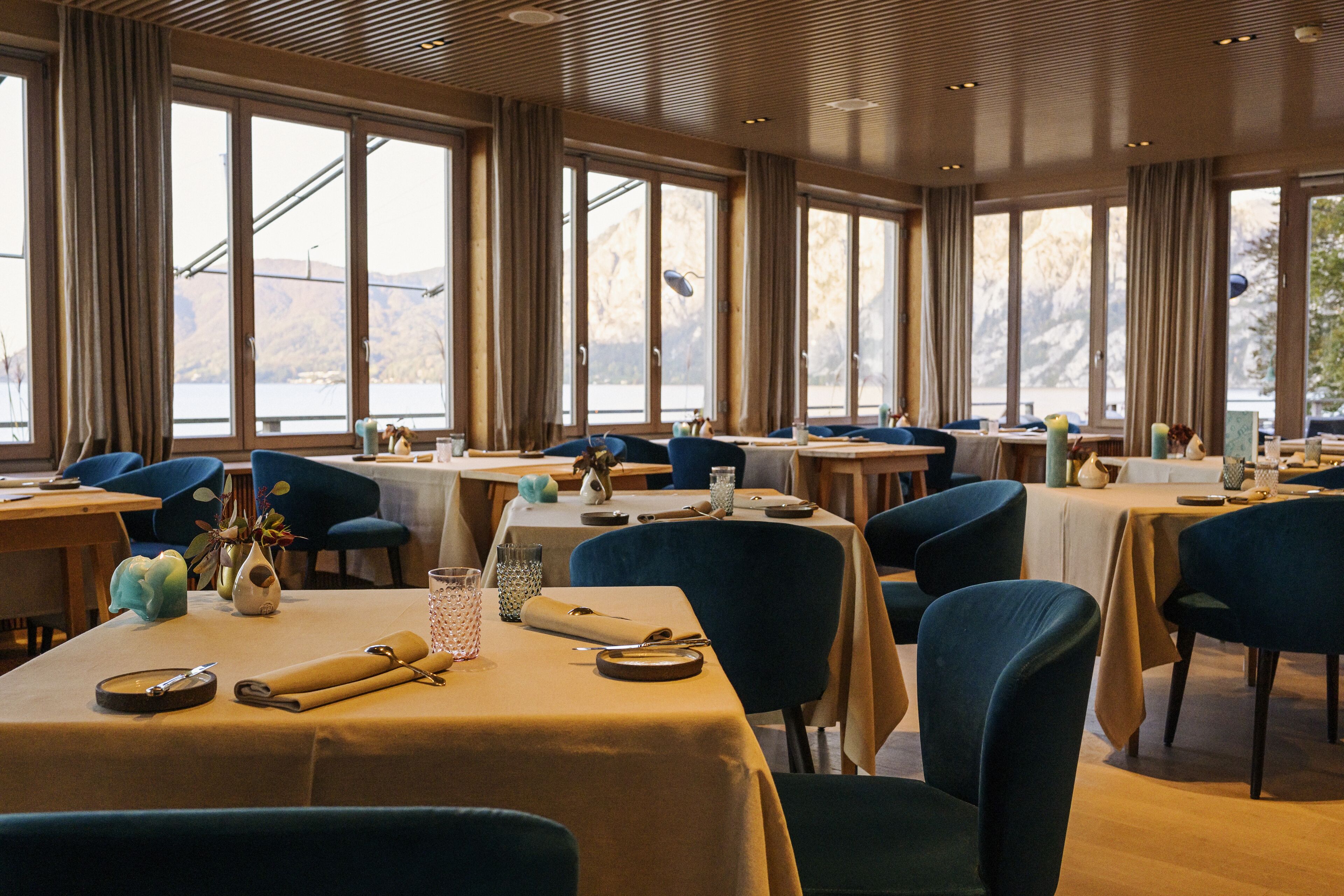 Un espace repas avec des tables dressées, de grandes fenêtres et des chaises bleues.