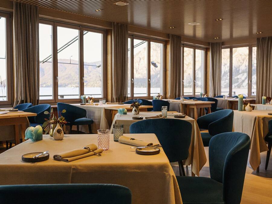 Un espace repas avec des tables dressées, de grandes fenêtres et des chaises bleues.