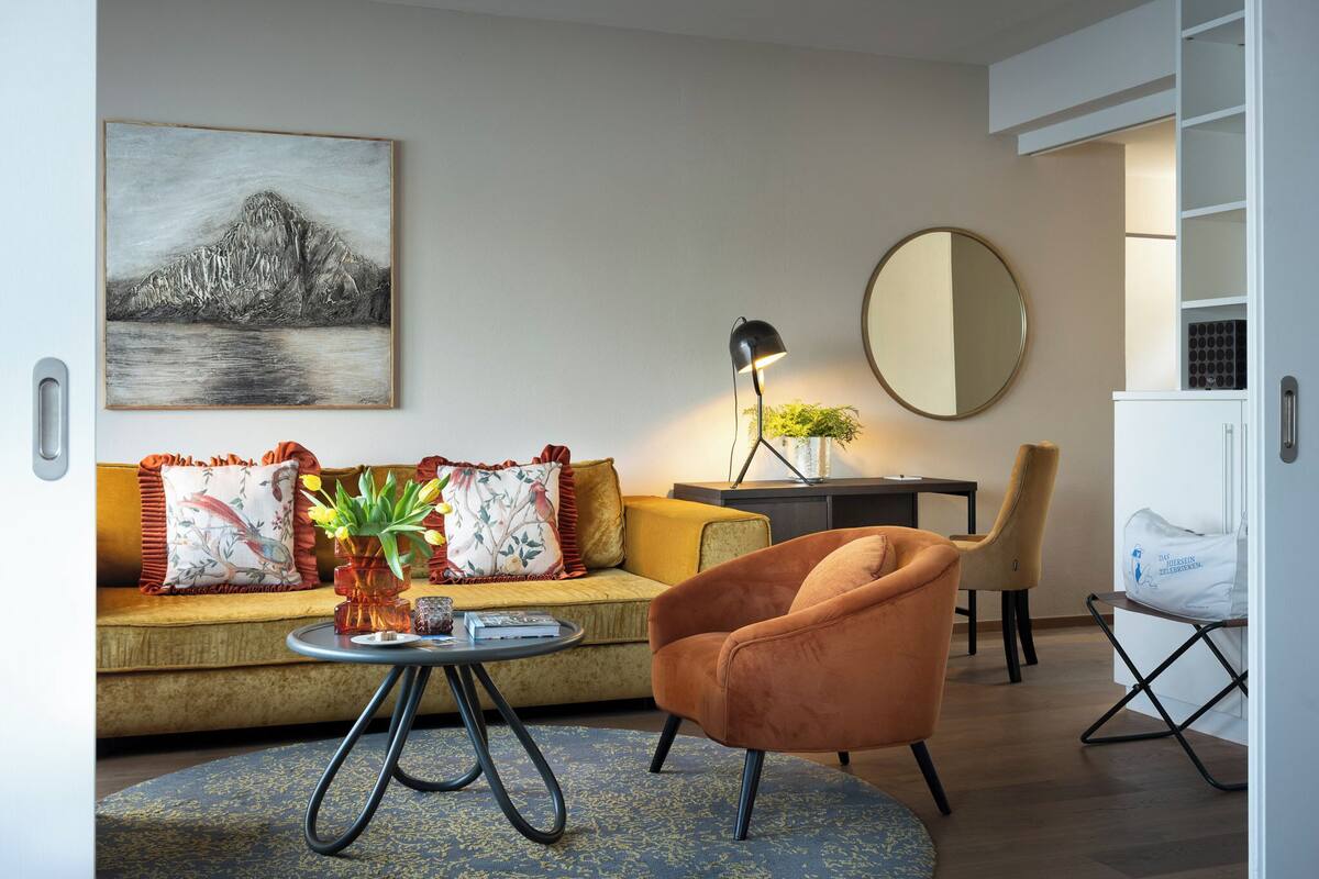 A living room with a sofa, armchair, coffee table, lamp, and a painting on the wall.