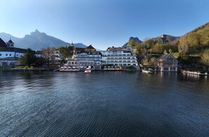 A lakeside hotel with a view of mountains, a dock with boats, and a large building with multiple floors.
