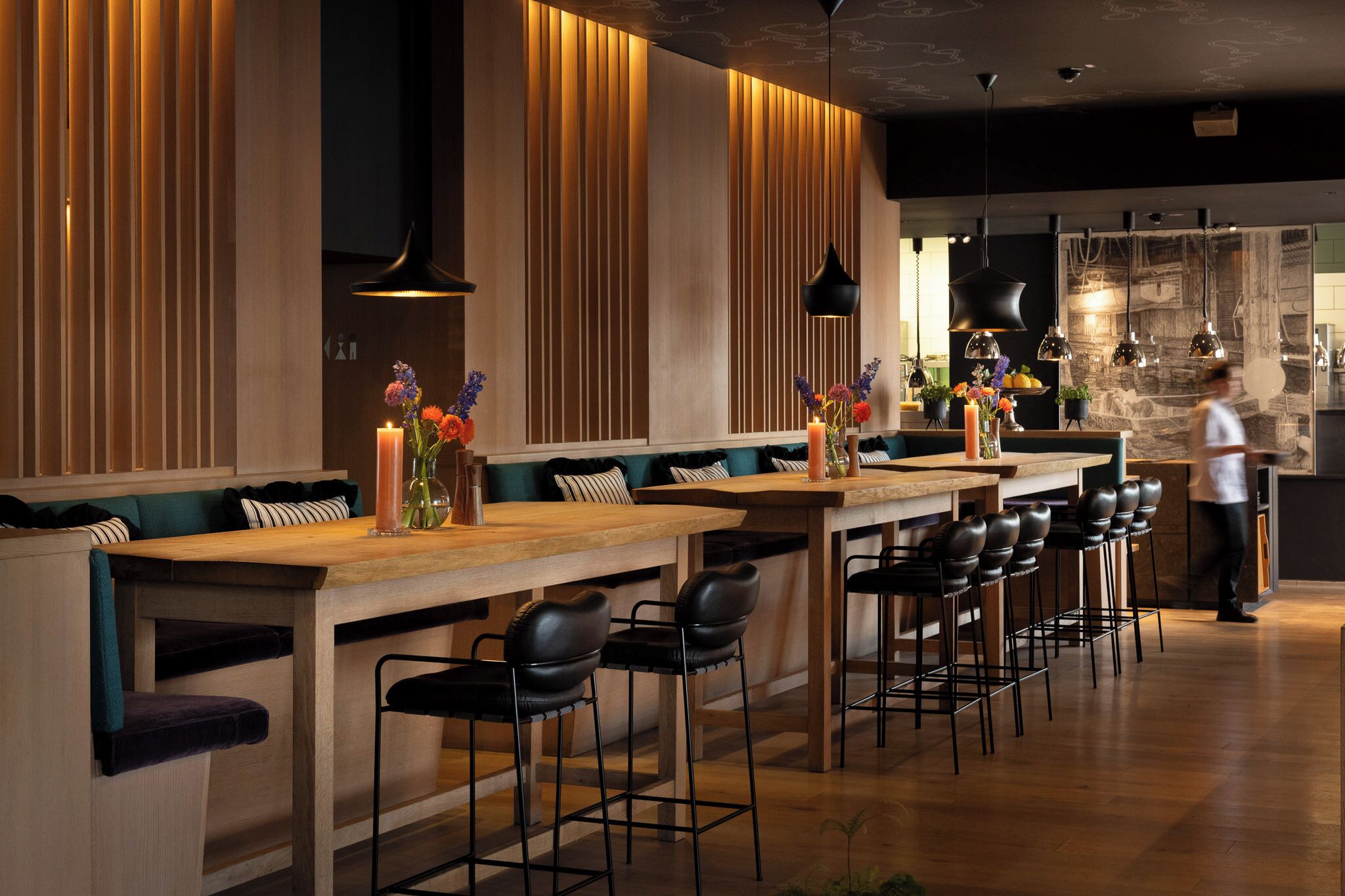 A modern bar area with wooden bar counters, black bar stools, and pendant lighting.