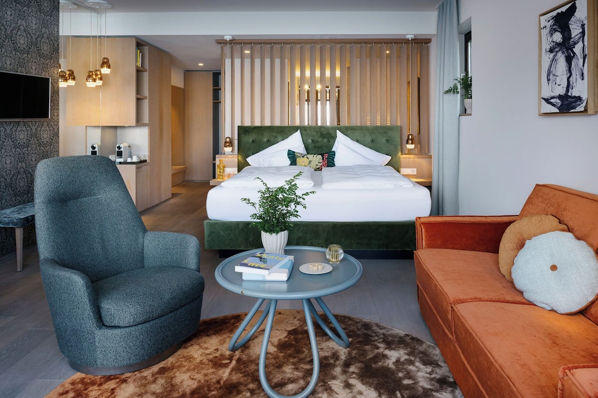 A modern hotel room with a bed, a sofa, a chair, a small table, and a TV.