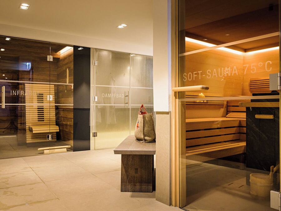 Un spa moderno con paredes de vidrio, bancos de madera y un cartel que indica una sauna suave a 75°C.