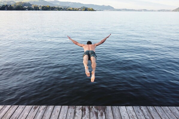A person jumping off a wooden dock into a body of water.