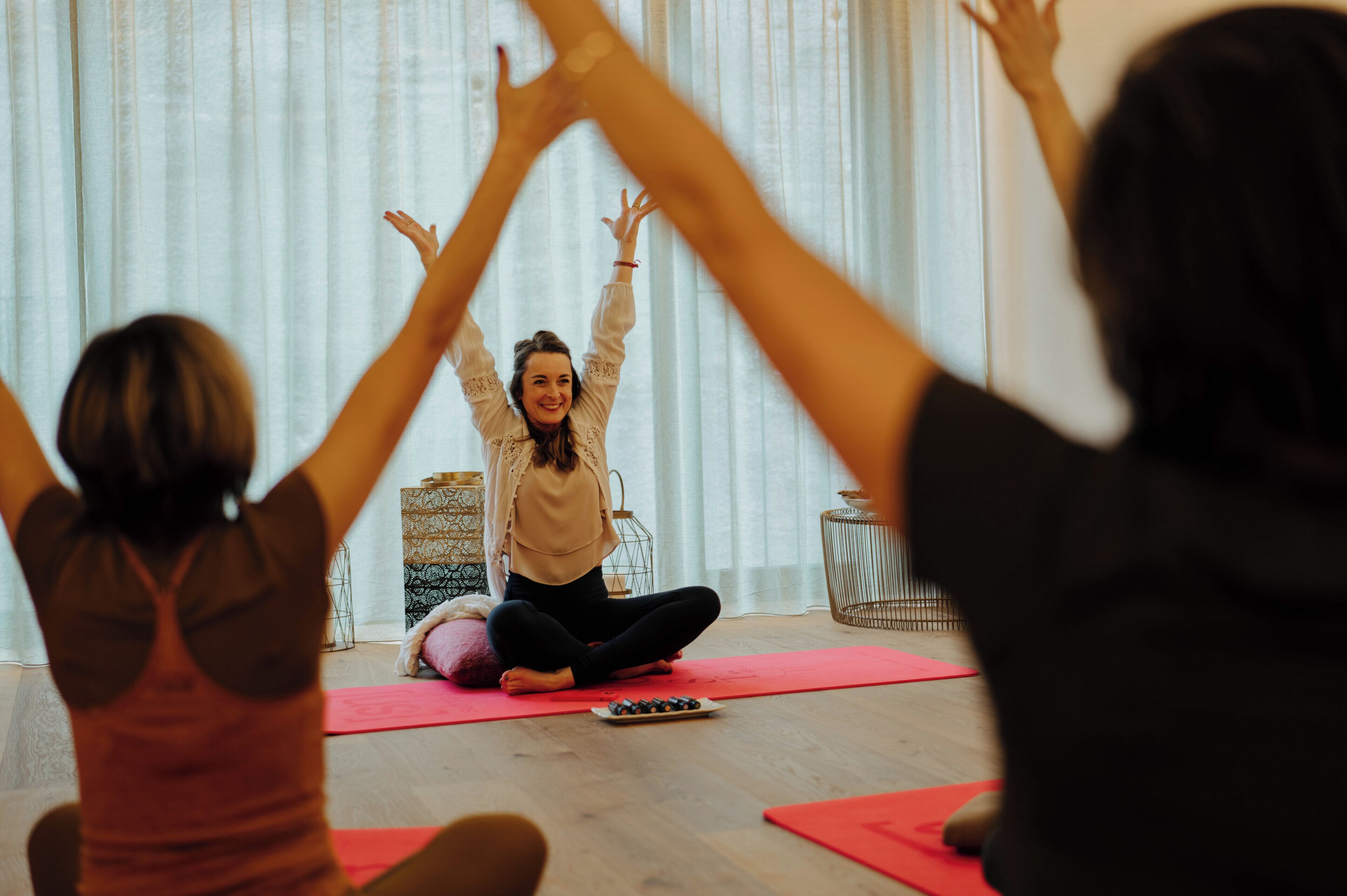Ein Yoga-Kurs in einem Raum mit Holzboden, Yogamatten und einem kleinen Tisch mit einer Schale Snacks.