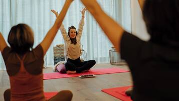 Ein Yoga-Kurs in einem Raum mit Holzboden, Yogamatten und einem kleinen Tisch mit einer Schale Snacks.