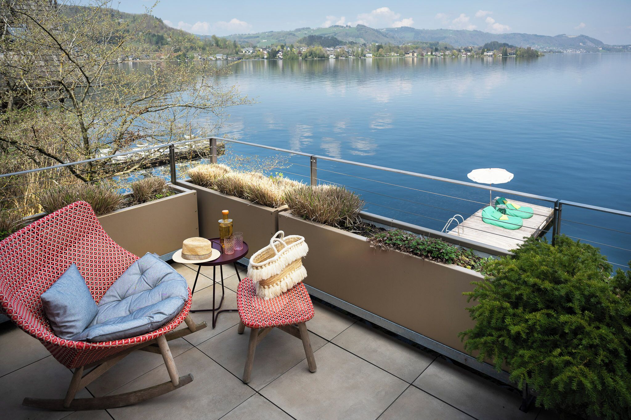 A balcony with a rocking chair, a small table with a hat, and a wicker basket.