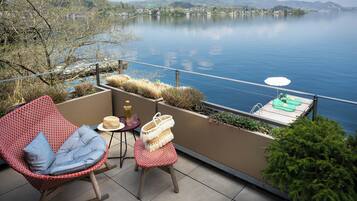 A balcony with a rocking chair, a small table with a hat, and a wicker basket.