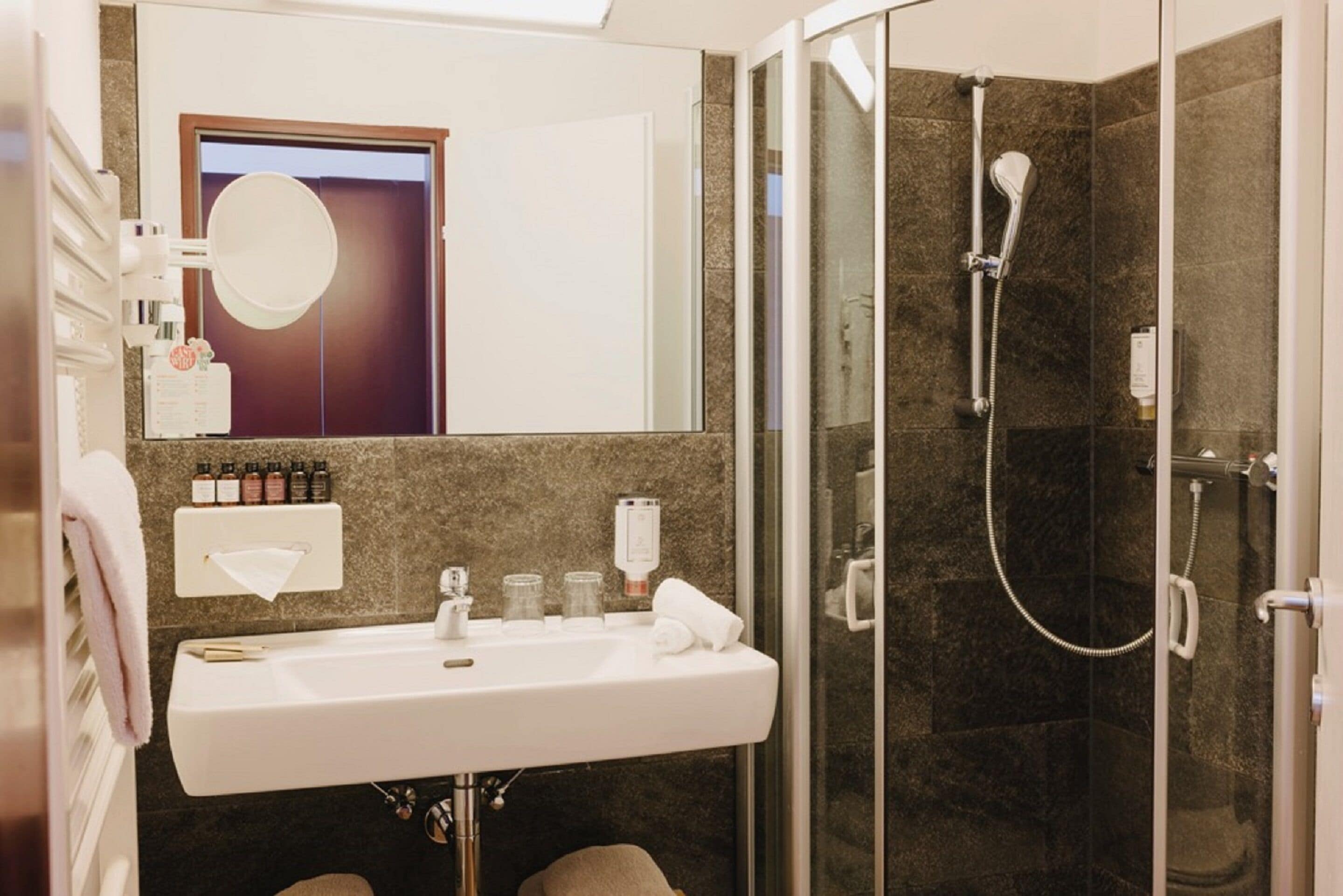 Un baño moderno con un lavamanos blanco, cabina de ducha con mampara de vidrio y un espejo sobre el lavamanos.