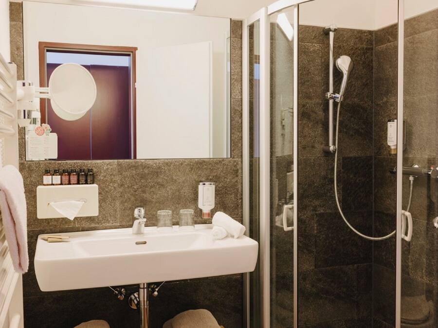 Un baño moderno con un lavamanos blanco, cabina de ducha con mampara de vidrio y un espejo sobre el lavamanos.