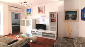 Un salon moderne avec un téléviseur à écran plat, des étagères blanches et un canapé.