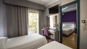 Une chambre d’hôtel avec deux lits, un bureau, une chaise, une télévision et une salle de bain visible à travers une porte ouverte.