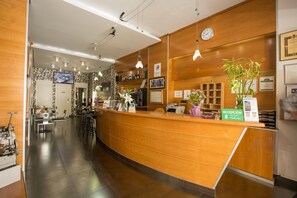 Un espace d’accueil d’hôtel avec un comptoir de réception en bois, une horloge et une enseigne indiquant « Réception ».
