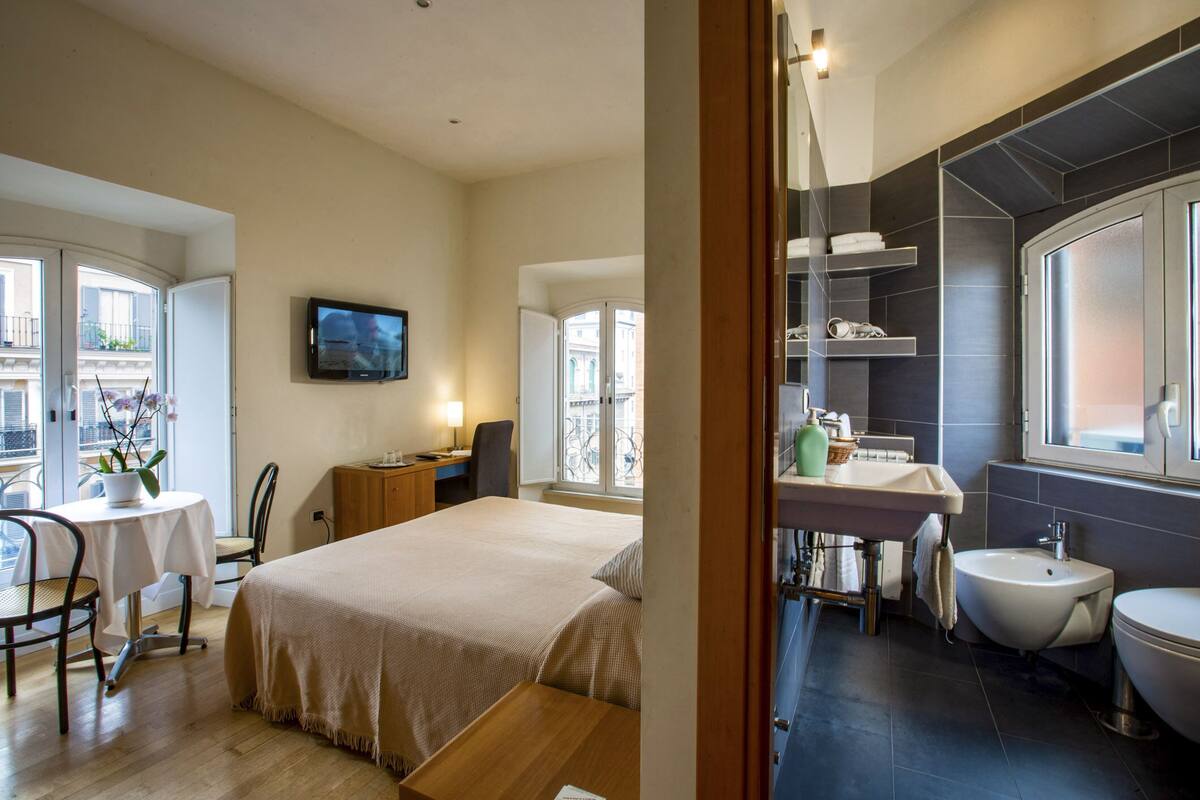 Une chambre d’hôtel comprenant un lit, un bureau, une chaise, une télévision et une salle de bain avec un lavabo, un bidet et une fenêtre.
